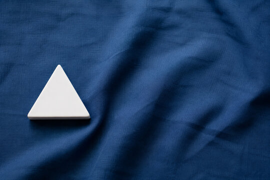 Single white equilateral triangle object on deep blue linen, calm still life for editorial concept