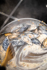 Mussels cooking in a creamy white wine sauce with garlic and herbs in a stainless steel pan on a stovetop. © pavel siamionov