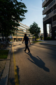 Pedestrian crosses a sunlit urban street between modern buildings in Nordbahnviertel Vienna Austria creating long shadows in a contemporary residential district