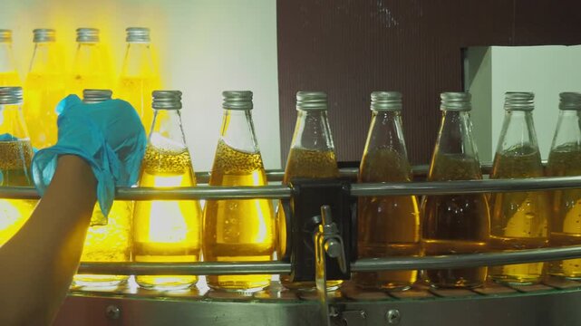 Quality control worker inspecting sealed beverage bottles on an automated conveyor belt in a modern industrial plant, ensuring hygiene, packaging integrity, and food safety standards.