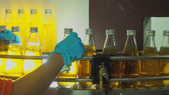 Quality control worker inspecting sealed beverage bottles on an automated conveyor belt in a modern industrial plant, ensuring hygiene, packaging integrity, and food safety standards.