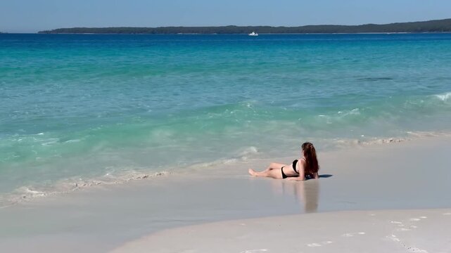 A girl in a bikini lies on the white sand of the famous Hyams Beach, gently washed by soft waves, near Wollongong, a paradise holiday destination, Jervis Bay, New South Wales, Australia.