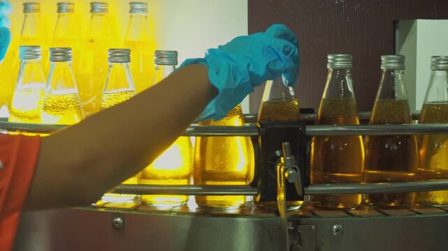 Quality control worker inspecting sealed beverage bottles on an automated conveyor belt in a modern industrial plant, ensuring hygiene, packaging integrity, and food safety standards.