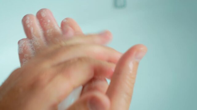 Soapy hands rubbing fingers together during thorough hand washing routine. Soap foam on wet skin for personal hygiene and infection prevention. Close up bathroom sanitation and cleanliness concept