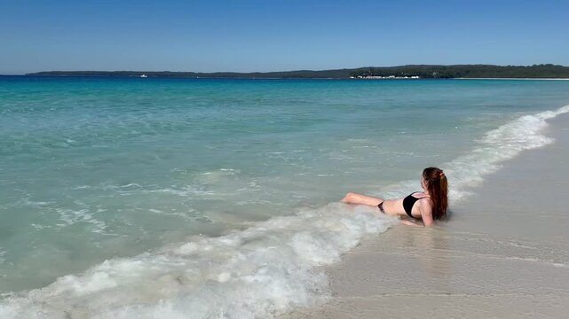 A girl in a bikini lies on the white sand of the famous Hyams Beach, gently washed by soft waves, near Wollongong, a paradise holiday destination, Jervis Bay, New South Wales, Australia.