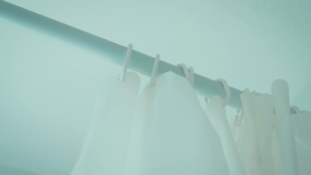 Close up of white shower curtain sliding along rod on plastic hooks as it is drawn shut. Bathroom privacy curtain closing around bathtub. Simple household routine and shower preparation concept
