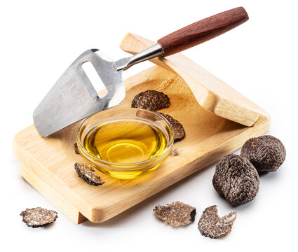 Glass bowl of luxury black truffle oil with fresh truffle slices and wooden slicer board and slicer knife. Clipping path, isolated on a white background.