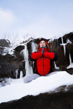 Woman sitting in lotus position and meditating on a snowy mountain rock with hands in namaste gesture. Winter mindfulness, meditation, solitude, wellness and connection with nature concept.