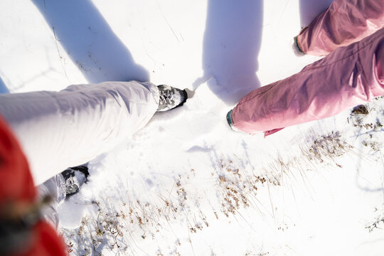 First-person view of people walking through a snow-covered winter landscape in warm outdoor clothing and hiking footwear. Sunny mountain trekking, active travel and outdoor adventure concept.