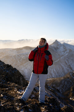 Female traveler with a backpack exploring a rocky mountain landscape in warm outdoor clothing during golden hour. Hiking, adventure tourism, wilderness exploration and active lifestyle concept.