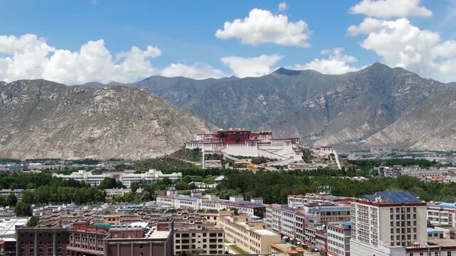 Potala Palace in Lhasa, Tibet, elevated cityscape with surrounding mountains and modern buildings under blue sky