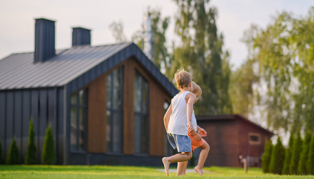 Young children running barefoot and playing together on green lawn near a modern house in warm evening sunlight. Active childhood, outdoor play, summer leisure and carefree lifestyle concept.