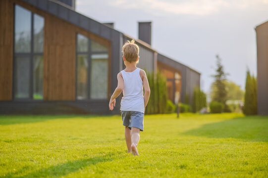 Young children running barefoot and playing together on green lawn near a modern house in warm evening sunlight. Active childhood, outdoor play, summer leisure and carefree lifestyle concept.