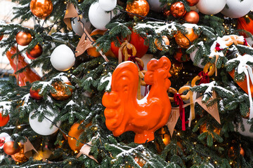 Winter Christmas tree with orange decorations, gifts, and a cockerel on a stick. Beautiful Christmas background. Concept for the New Year 2027.  © Юлия Клюева