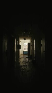 Gloomy old dormitory hallway with natural light from distant window at end. Eerie quiet residential interior.Dark old dormitory corridor with daylight from window at end. Vertical video.