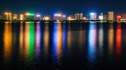 Fototapeta premium Night cityscape skyline with bright colorful lights reflecting on calm water surface. Urban buildings glow in many colors across dark horizon. Vibrant city lights shimmer on lake ripples during