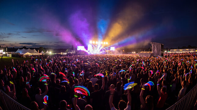Silhouetted festival crowd waving glow stick bracelets at night concert