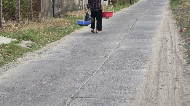 Vietnamese rural scene with a local vendor carrying a traditional shoulder pole walking on a concrete road in Central Vietnam