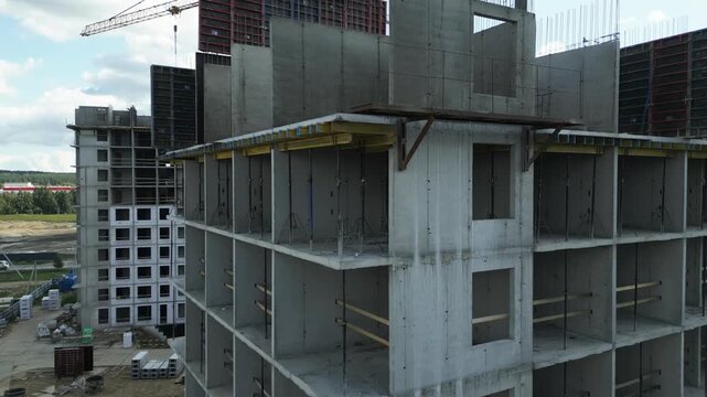 Unfinished multistory concrete building corner with repeating room openings grid, with crane on the back