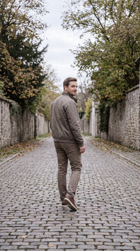 Man walking alone down a quiet cobblestone alley lined with autumn trees