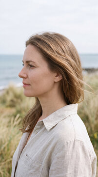 Woman in profile with windblown hair standing quietly beside the ocean
