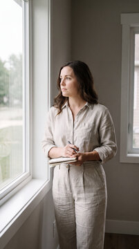 Woman standing by a window looking outward in quiet, thoughtful contemplation