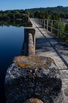 Close up of weathered stone railing pillar with lichen on pedestrian bridge over calm lake