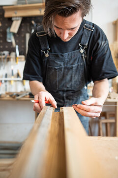 Carpenter making measurements for patch replacement on vintage wooden window frame in repair shop, man crafter carefully examining and measuring fitting of material, using ruler tool and pencil.