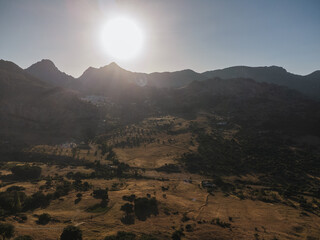 Aerial view of rugged mountain peaks rising above a dry valley with scattered vegetation and terraced fields under bright sunlight in Grazalema, Spain © Felix Morion