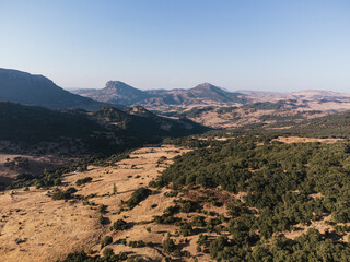 Aerial view of rugged mountain peaks rising above a semi-arid valley with scattered green vegetation and golden dry grassland under a clear blue sky in Grazalema, Spain © Felix Morion