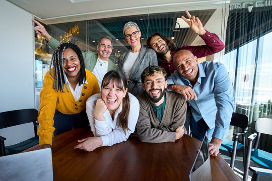 Multicultural coworkers laughing during a lively office meeting, showcasing teamwork, friendship, success, and a vibrant corporate atmosphere.