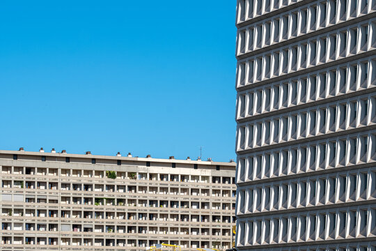 Buildings and facade geometry create abstract urban architecture against blue sky with pattern repetition and open exterior space