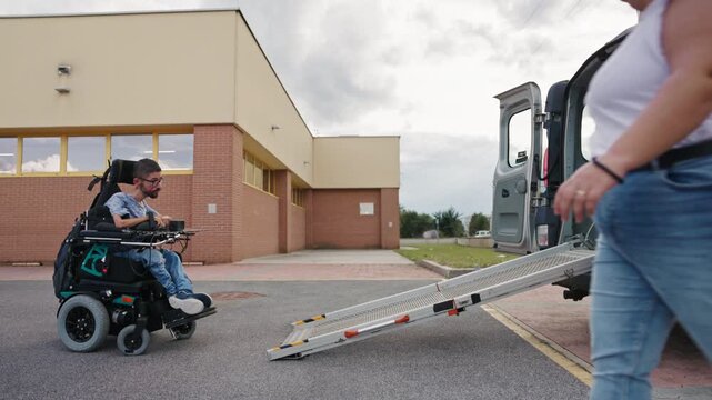 Personal assistant accompanying a powered wheelchair user into an adapted vehicle using an accessible ramp.