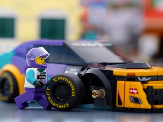 Fototapeta premium Tambov, Russian Federation - January 02, 2026 Lego NASCAR driver minifigure next to a purple and yellow Chevrolet Camaro race car during a pit stop with a detached wheel.