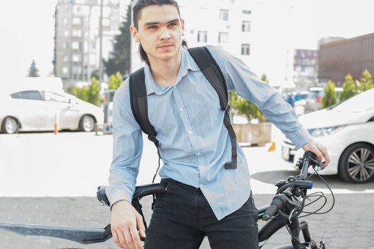A young man with long hair sits on a bike in a city area.