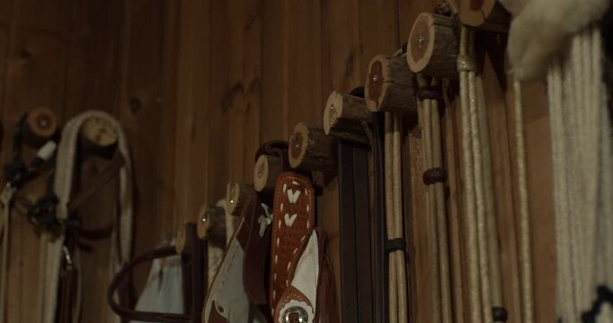 Western saddles and riding tack hang neatly against a wooden wall in a Texas barn, creating a rustic equestrian equipment background for ranch and cowboy themes.