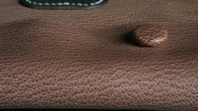 Extreme close up leather notebook cover with button closure, textured surface. Detailed leather pattern, tactile material, stationery accessory. Leather notebook case with button clasp macro view 