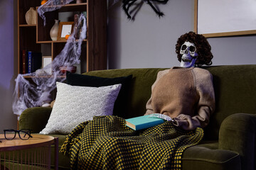 Halloween humor and waiting concept, skeleton wearing a sweater and wig sitting on a sofa with a...