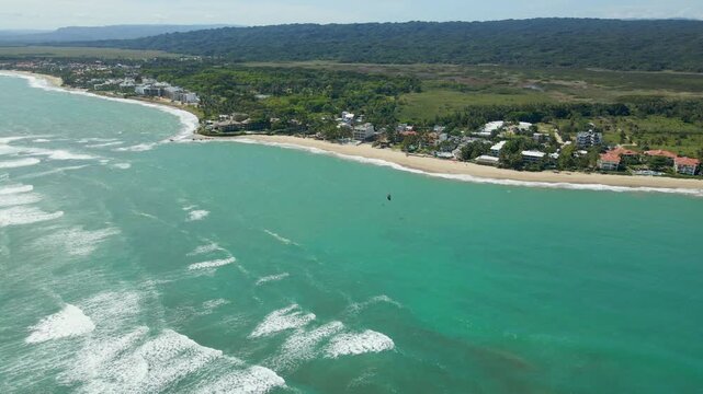 Kite surfer sailing on turquoise water near the sandy coastline of cabarete, a popular water sports destination.