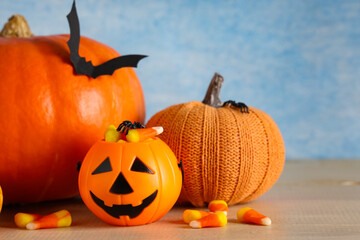 Naklejka premium Halloween celebration and autumn holiday traditions, jack-o-lantern candy bucket with pumpkins and candy corn on a wooden table against a blue background
