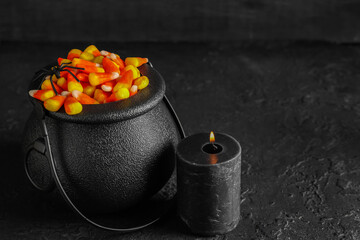 Naklejka premium Halloween celebration and trick or treat tradition, candy corn in black cauldron with spider and burning candle on dark textured background