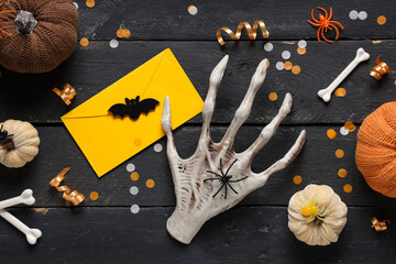 Naklejka premium Halloween party invitation, spooky skeleton hand with yellow envelope and festive autumn decorations on dark wooden background for holiday celebration