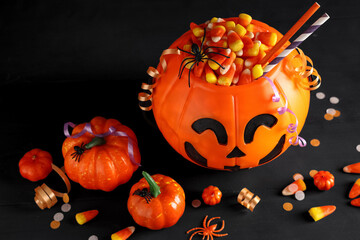 Naklejka premium Halloween celebration and trick or treat tradition, pumpkin candy bucket filled with candy corn and plastic spiders on a dark wooden background
