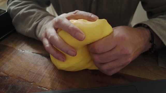 Man repeatedly squeezes a soft ball while sitting at a home desktop, evoking workplace stress, concentration, relaxation and tactile coping strategies.
