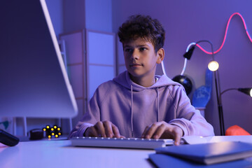 Digital childhood and remote learning, teenage boy using computer for online education and gaming in a dark room with neon lighting at night © Pixel-Shot