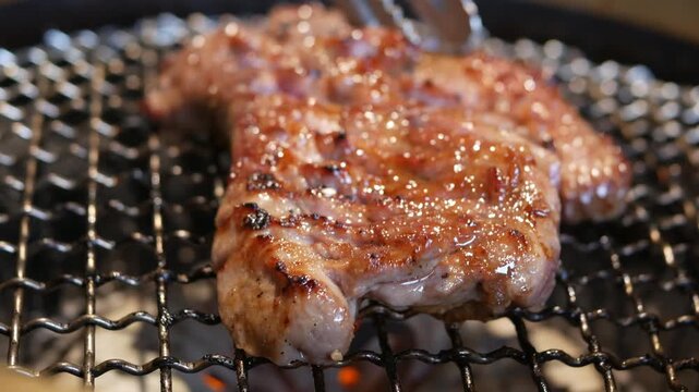 Close-up shot of grilled pork on a stainless steel mesh over a charcoal grill with bursting flames.