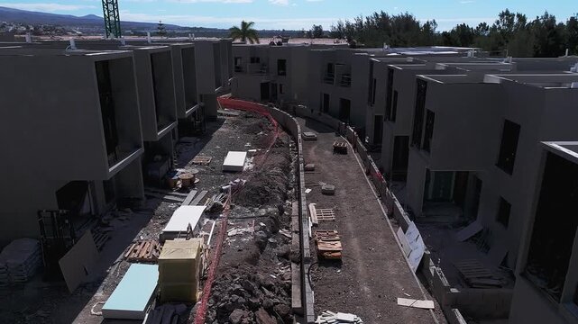Aerial view of a modern residential construction site with partially completed apartment buildings, unfinished access roads and building materials showing ongoing development progress