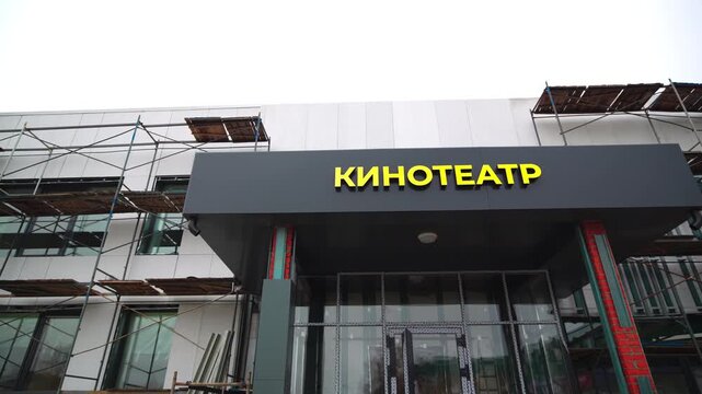 Empty scaffolds by facade of unfinished cinema building in city district. Urban construction site of entertainment center for movie watching