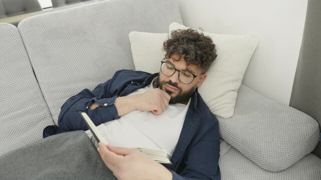 Young man falling asleep while reading book on the sofa
