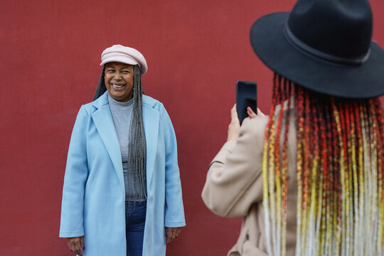 African american daughter taking a photo with smartphone of trendy mother in the city during autumn season - Fall lifestyle, family and travel concept